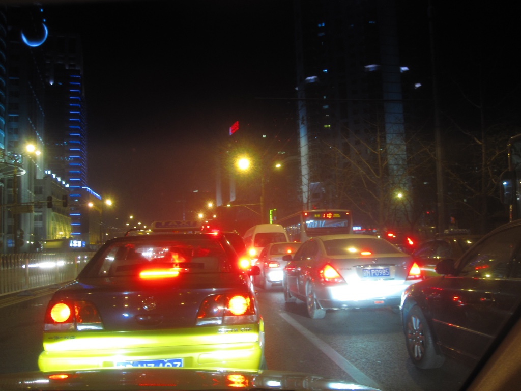 A photograph taken from the front seat of a taxi through the windsheild. It is night time adn all the cars ahead have their red lights shining. 