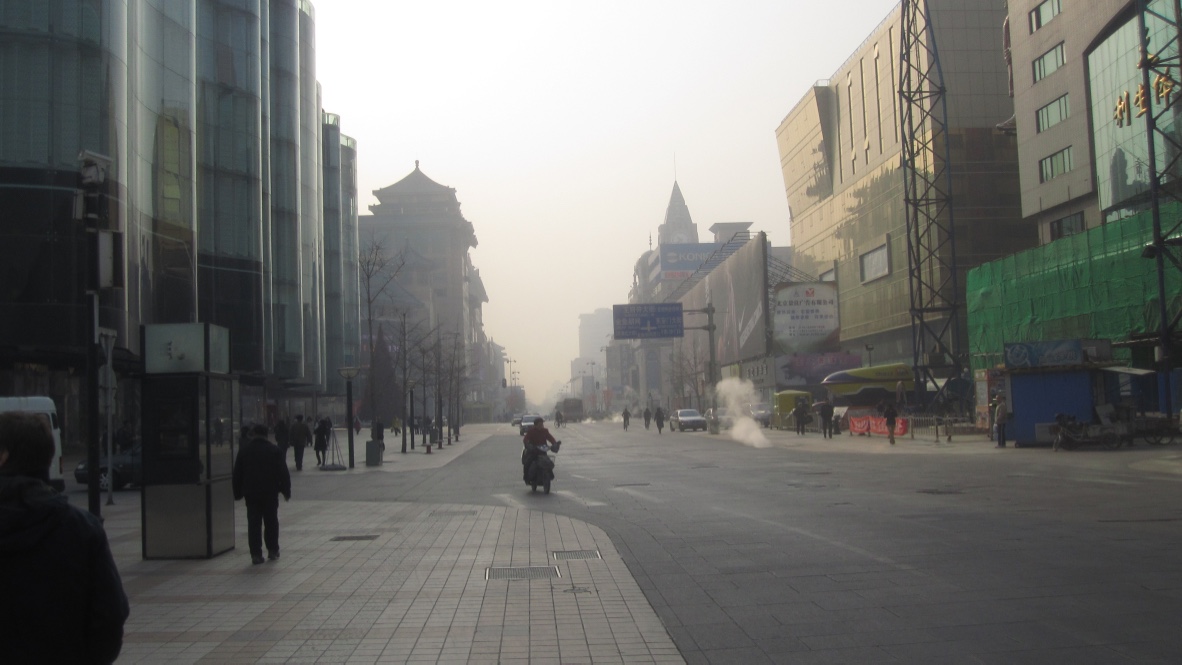 A lone motorscooter rider on a broad deserted Bejing street.