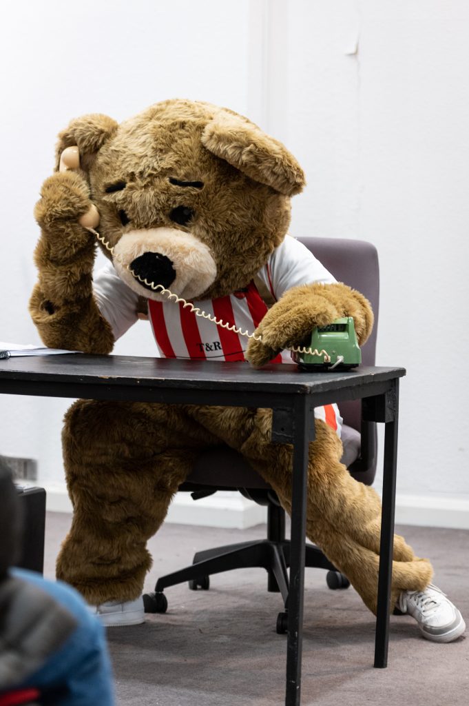 A football mascot bear at an office desk on teh telephone.